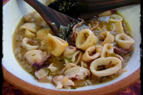 Calamares en salsa, un plato casero con trozos tiernos y tentáculos, servido en un cuenco de barro.