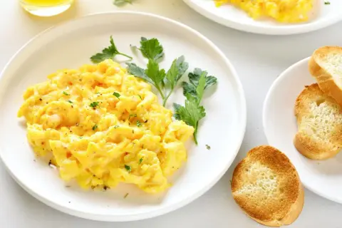Un plato de huevos revueltos esponjosos, adornado con perejil fresco y acompañado de tostadas crujientes.