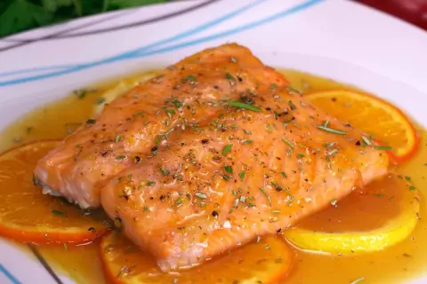 Delicioso salmón a la naranja, bañado en salsa cítrica y adornado con rodajas de naranja y hierbas frescas.