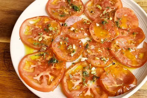 Delicioso carpaccio de tomate con aceite de oliva, ajo picado, hierbas frescas y trocitos de pistacho.
