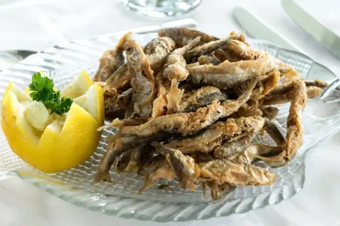 Deliciosa fritura de pescado crujiente servida en un plato con forma de pez, acompañada de limón tallado y perejil fresco.