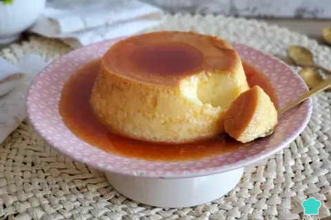 Un delicioso flan de leche condensada, con una porción servida en cuchara dorada, bañado en caramelo líquido.