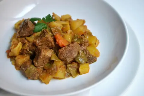 Un plato de carne guisada con patatas, zanahorias y pimientos verdes, adornado con perejil fresco.