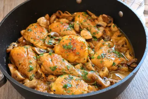 Pollo a la cerveza jugoso y dorado, con champiñones y perejil fresco, servido en una sartén.