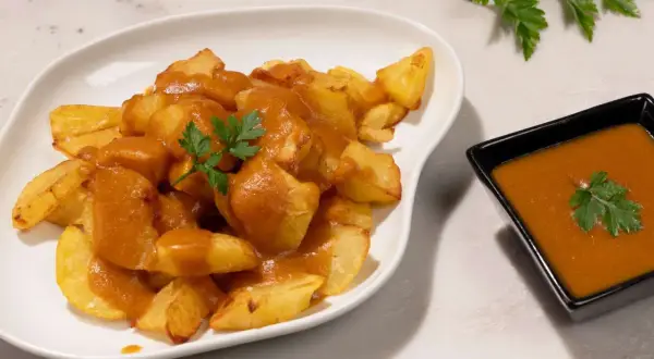 Patatas bravas crujientes cubiertas con salsa picante y perejil fresco. Un plato español delicioso.