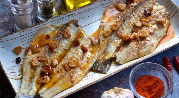 Dos filetes de lubina a la bilbaina, dorados y jugosos, con láminas de ajo crujiente y guindilla.