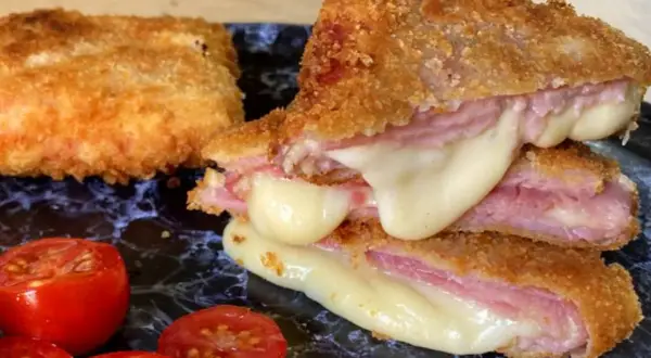 San Jacobo crujiente con queso fundido y jamón, acompañado de tomates cherry.