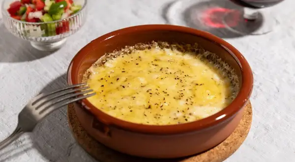 Delicioso provolone al horno burbujeante, servido en cazuela de barro con una guarnición de pimientos y una copa de vino tinto.