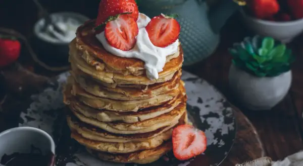 Pila de tortitas esponjosas cubiertas con nata y fresas. Una deliciosa receta de tortitas para el desayuno.