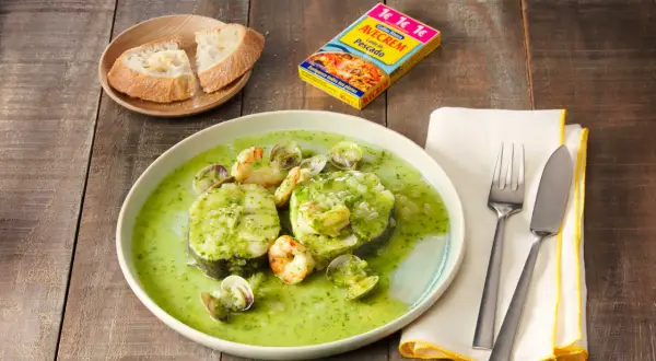 Merluza a la vasca con gambas y almejas en salsa verde, acompañada de pan.