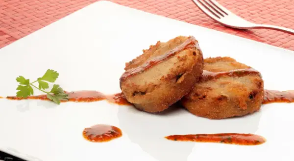 Dos porciones de manitas de cerdo rebozadas y fritas, servidas con salsa roja y perejil en un plato blanco.