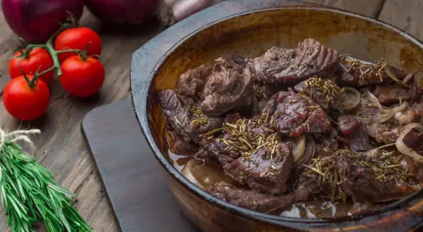 Carrilleras de ternera estofadas con romero y cebolla, servidas en cazuela de barro.