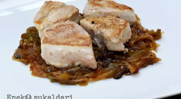Cuatro trozos de bonito encebollado, jugosos y dorados, reposan sobre una cama de cebolla caramelizada y pimientos verdes.