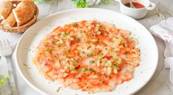Delicioso carpaccio de gambas con aderezo y hierbas frescas, servido con panecillos.