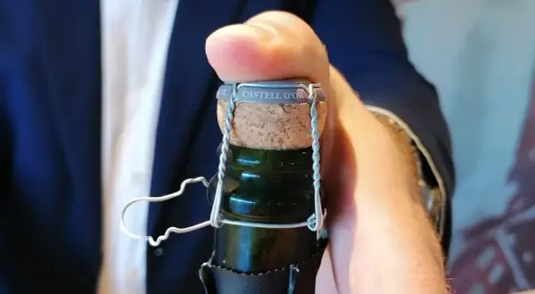 Dedo presionando el corcho de una botella de cava "CASTELL D'OR". Aprende como abrir una botella de vino espumoso.