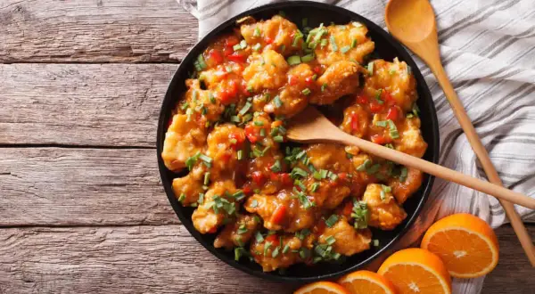 Delicioso pollo a la naranja, crujiente y bañado en una salsa dulce y cítrica, adornado con cebollín fresco.