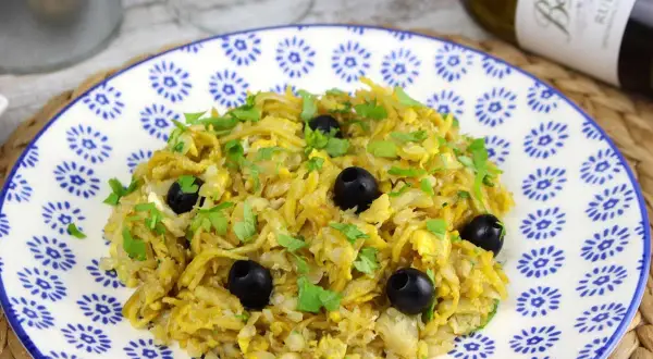 Delicioso bacalao a bras, un plato tradicional con patatas finas, huevo y aceitunas negras, espolvoreado con perejil fresco.