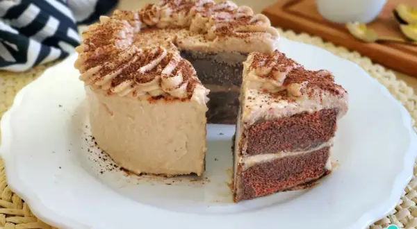 Deliciosa tarta de moka con crema y cacao espolvoreado. Un trozo cortado revela sus capas de bizcocho y relleno.