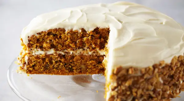 Delicioso pastel de zanahoria con glaseado cremoso y nueces picadas en los bordes.