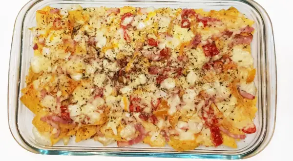 Nachos con queso recién horneados, cubiertos con trozos de tocino y pimientos rojos.