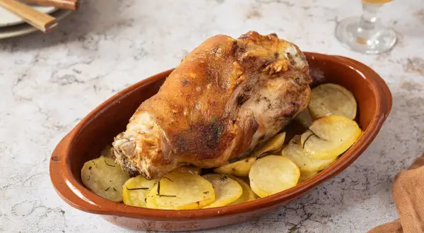 Codillo de cerdo asado, crujiente y dorado, servido en cazuela de barro con patatas panadera.