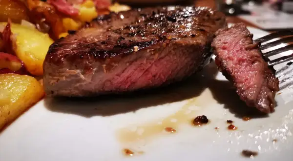 Un jugoso entrecot de ternera a la parrilla, servido con patatas doradas y un tenedor listo para degustar.
