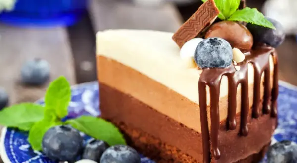 Deliciosa tarta tres chocolates en un plato azul, decorada con arándanos y menta.