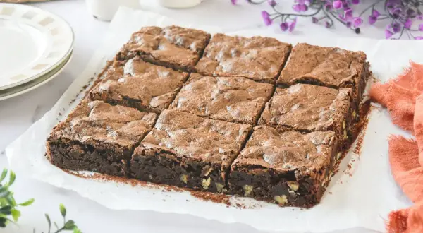 Un delicioso brownie sin gluten, cortado en nueve porciones, espolvoreado con cacao y con trozos de nuez visibles.