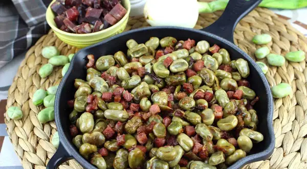 Habitas tiernas salteadas con trocitos de jamón crujiente en una sartén de hierro fundido. Un plato casero y delicioso.