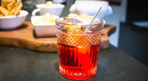 Cóctel rojo vibrante, una mezcla de vermut rojo y blanco, con guarnición de limón.