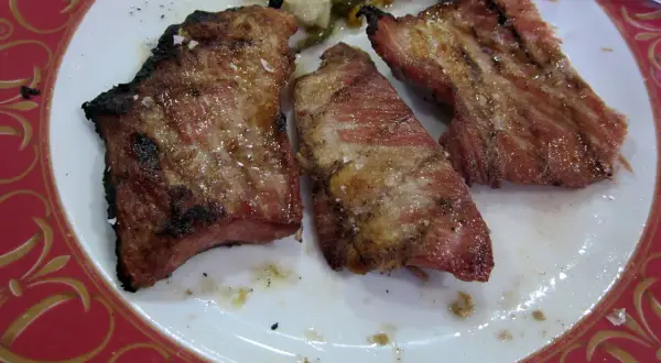 Tres jugosas porciones de secreto ibérico a la parrilla, con sal gruesa y un toque de pimienta, servidas en un plato blanco con borde decorado.