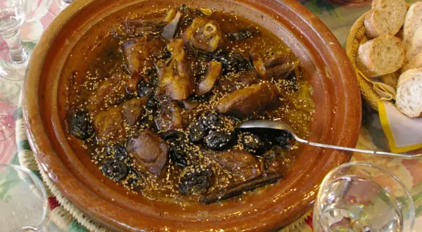 Un delicioso tajine de cordero con ciruelas pasas y semillas de sésamo, servido en una cazuela de barro.