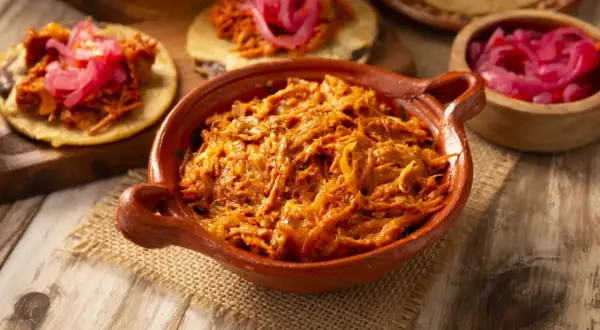 Cochinita pibil en cazuela de barro, lista para servir en tortillas con cebolla morada encurtida. ¡Un festín de sabor!