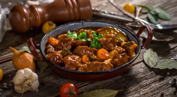 Un delicioso caldereta de cordero, con trozos tiernos de carne, zanahorias y brócoli, servido en una cazuela rústica.