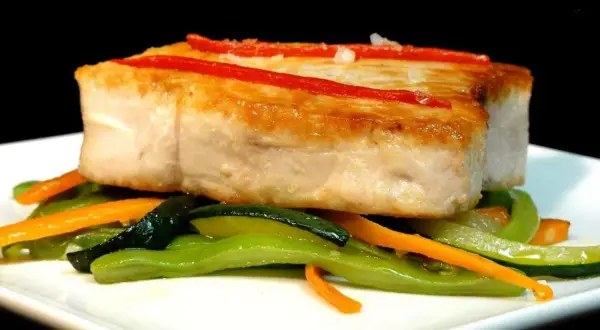 Bonito jugoso sobre verduras salteadas, con tiras de pimiento rojo.