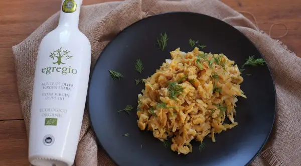Un plato de revuelto de bacalao con eneldo fresco, acompañado de una botella de aceite de oliva virgen extra ecológico Egregio.