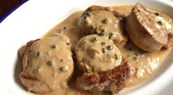 Cuatro medallones de solomillo a la pimienta, cubiertos con una cremosa salsa de pimienta verde, servidos en un plato blanco.