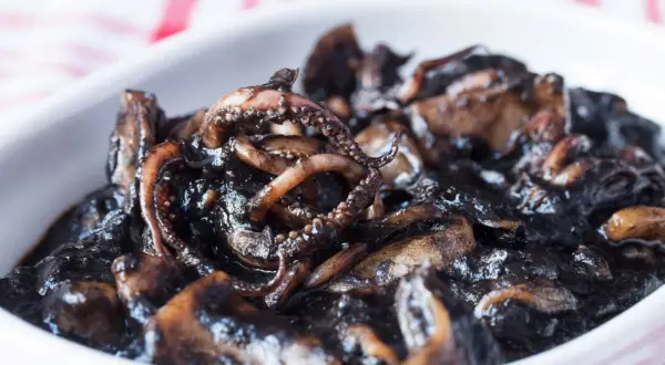 Un plato de calamares en su tinta, con tentáculos visibles y una salsa oscura y brillante.