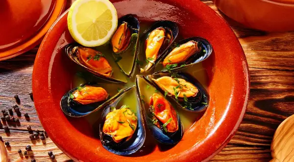 Mejillones al vapor servidos en un cuenco de barro con limón y perejil.