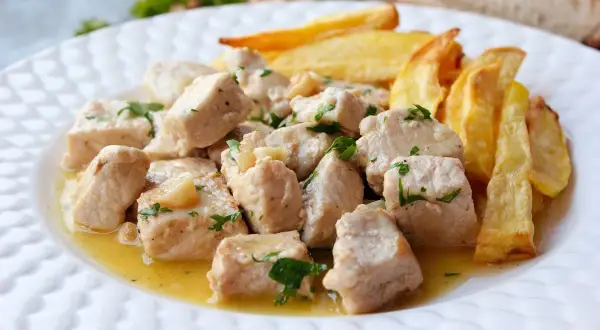 Sabroso lomo al ajillo en trozos, bañado en aceite y ajo, con patatas fritas doradas al lado.