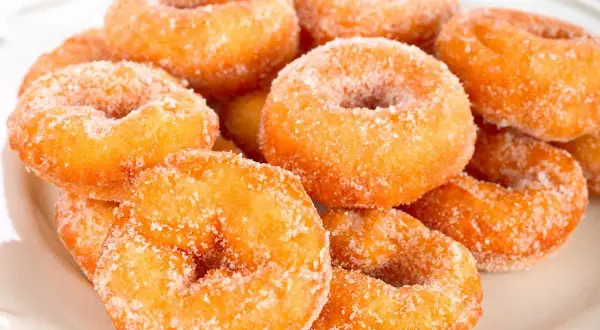 Montón de rosquillas caseras de toda la vida, doradas y espolvoreadas con azúcar, listas para disfrutar.