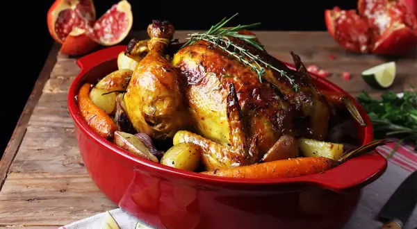 Pollo asado dorado con patatas y zanahorias, perfecto para tus recetas con pollo. Acompañado de granada y lima.