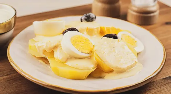Papa a la huancaina servida en un plato blanco, con rodajas de huevo duro y aceitunas negras.