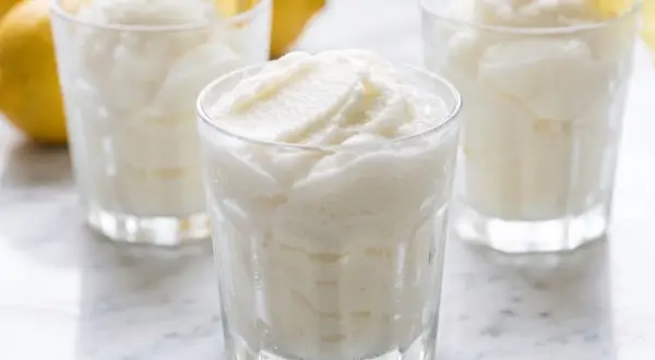 Tres vasos de sorbete de limón refrescante, con limones amarillos y hojas de menta en el fondo.