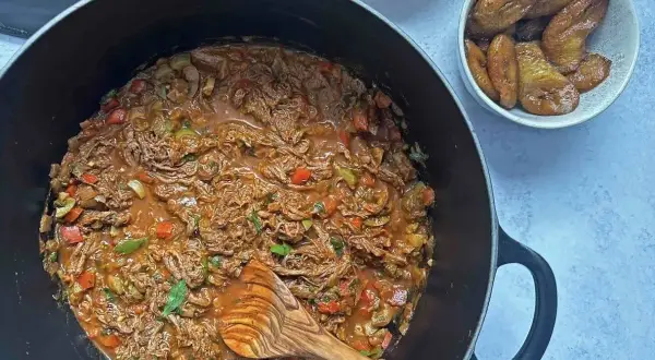 Un delicioso plato de ropa vieja, con trozos de carne deshebrada en salsa roja, acompañado de plátanos maduros fritos y arroz blanco.