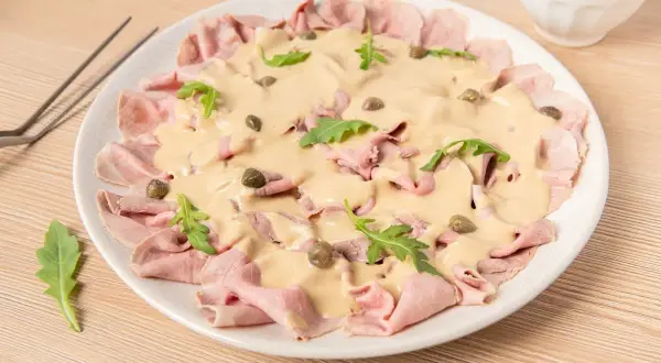Delicioso vitello tonnato con finas lonchas de ternera, salsa cremosa, alcaparras y rúcula. Un plato italiano clásico.