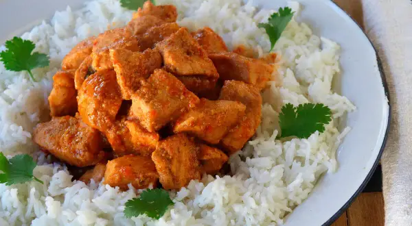 Sabroso pollo tikka masala cubierto con arroz blanco y decorado con cilantro fresco.