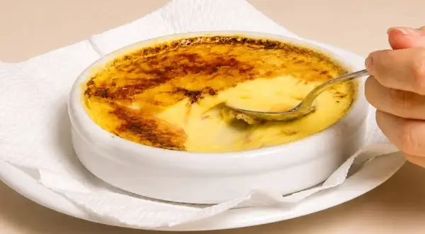 Una cuchara se hunde en un cremoso creme brulee con una capa superior caramelizada y dorada.