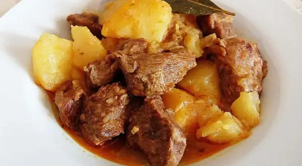 Plato de morcillo de ternera estofado con patatas y una hoja de laurel.