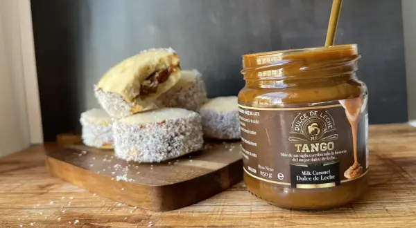 Alfajores cubiertos de coco y un frasco de dulce de leche Tango, listos para disfrutar.
